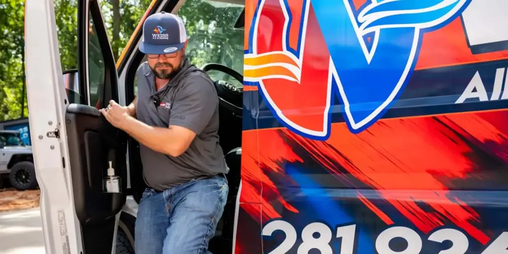 A uniformed Weiss Air Conditioning & Plumbing technician wearing a logo cap steps out of a company van.