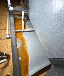 AC drain pan with standing water and rust buildup, indicating a clogged or leaking air conditioner