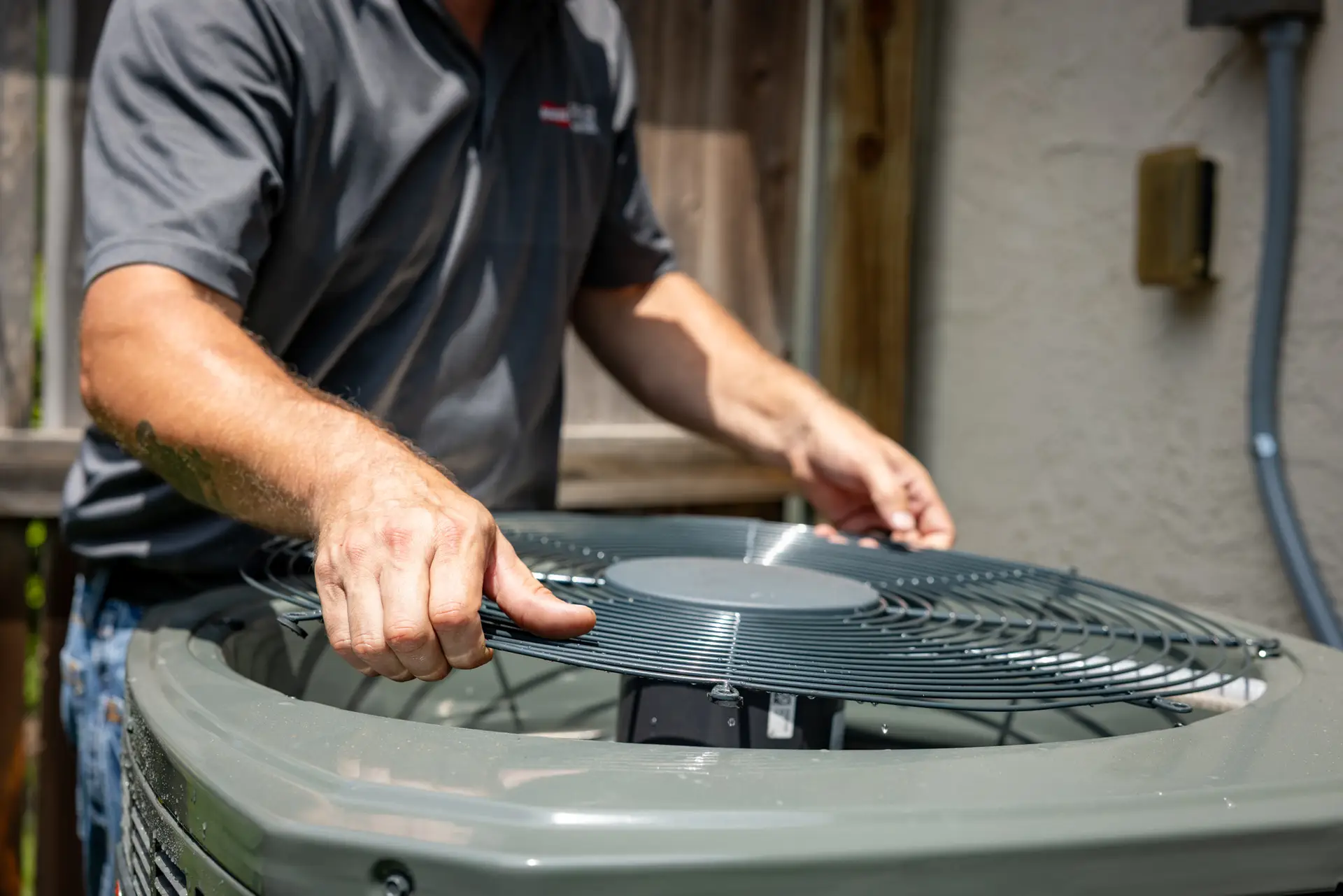 HVAC technician performing preventative maintenance by inspecting and servicing an outdoor AC unit fan.