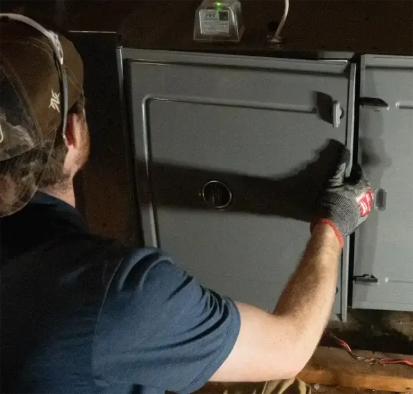A weiss technician wearing a cap and gloves is servicing a heating unit, focusing on the front panel of the furnace. Performing heating maintenance and heating services.