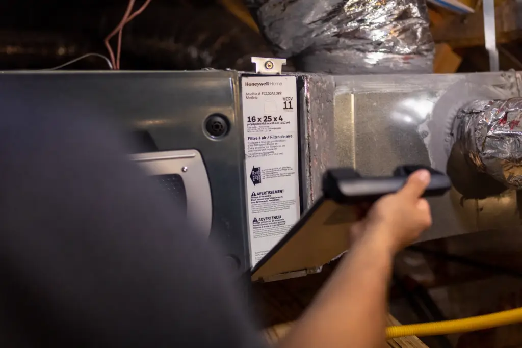 HVAC technician is changing a filter in the attic.