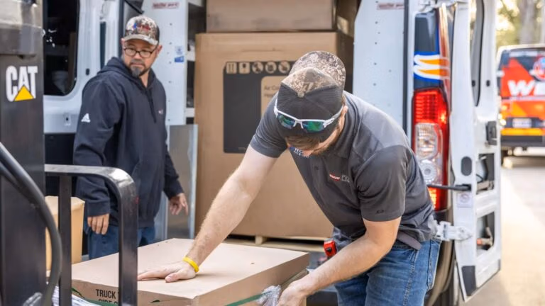 Two Weiss AC & Plumbing workers loading boxes from van