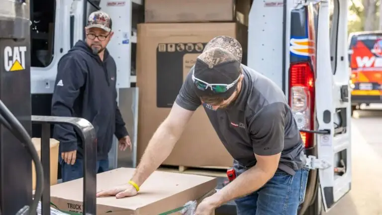 Two Weiss AC & Plumbing workers loading boxes from van