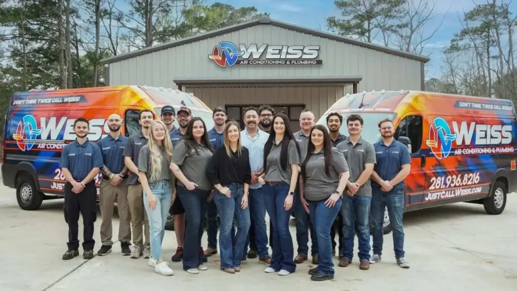 Team of Weiss Air Conditioning & Plumbing technicians and staff standing in front of company building and two branded service vans.