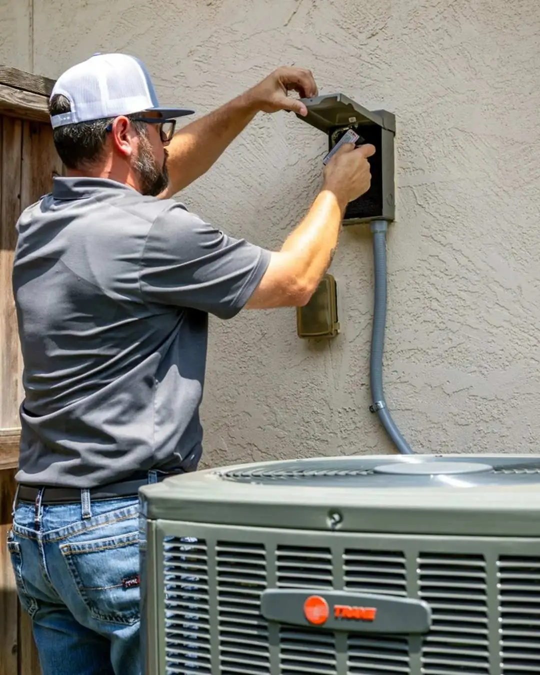 A Weiss Air Conditioning & Plumbing technician inspecting the outdoor electrical disconnect box and fuses for a Trane AC unit in Conroe.