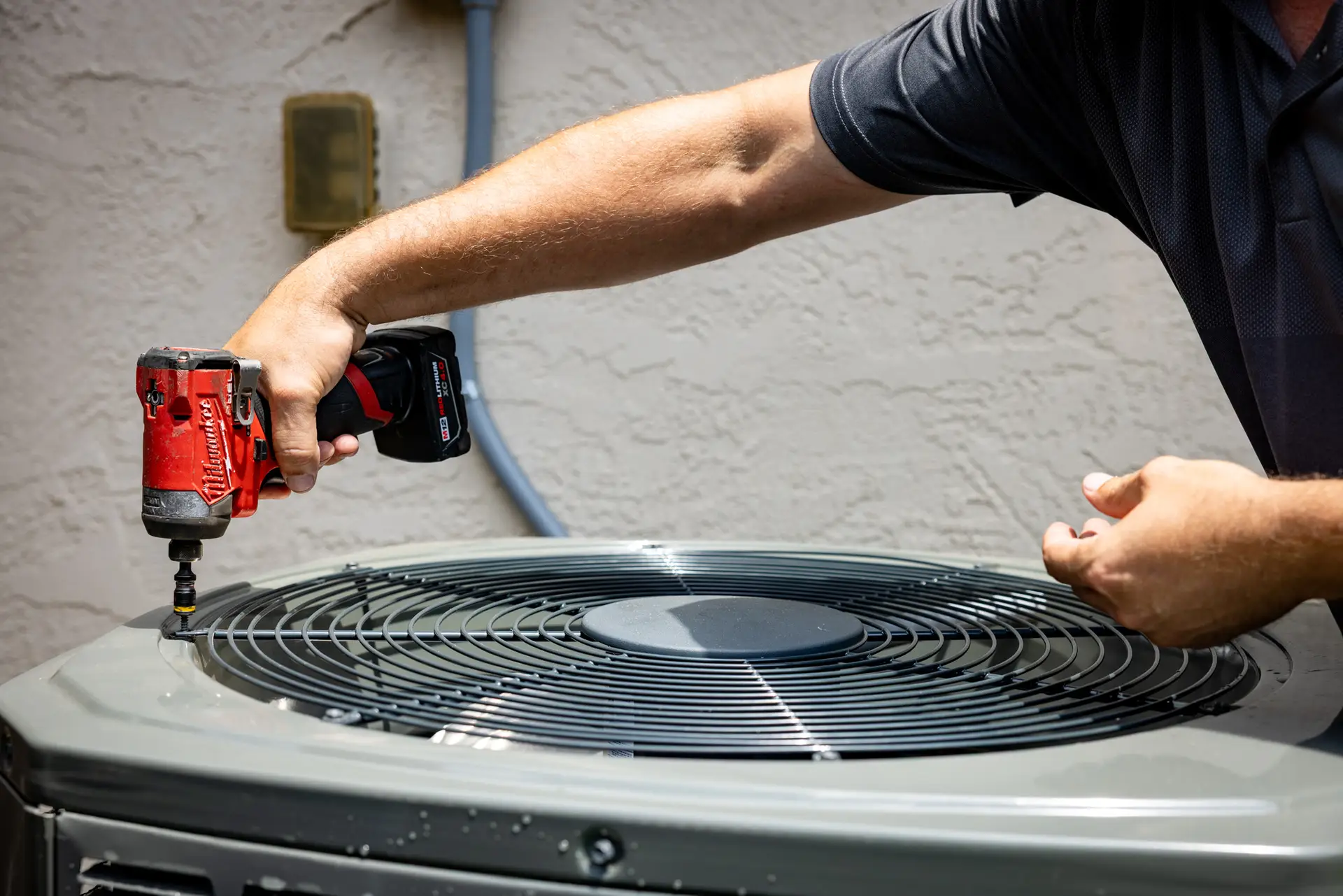 An HVAC technician using a power drill to repair an outdoor air conditioning unit in Montomery, TX.