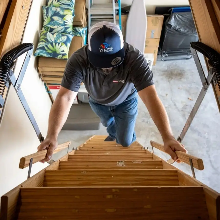 Weiss Air Conditioning & Plumbing technician climbing a wooden pull-down ladder to perform a professional attic HVAC system inspection.