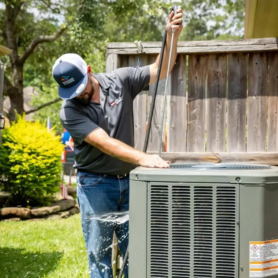 A Weiss Air Conditioning & Plumbing technician cleaning and prepping an outdoor condenser unit during a maintenance in Montgomery County