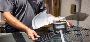 An HVAC technician inspecting and servicing a condenser fan motor assembly during a routine AC maintenance visit in Conroe, TX.