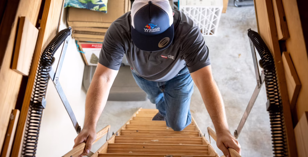Weiss A/C & Heating technician climbing attic stairs to perform heater maintenance and a pre-winter furnace tune-up in a home in Conroe, TX.